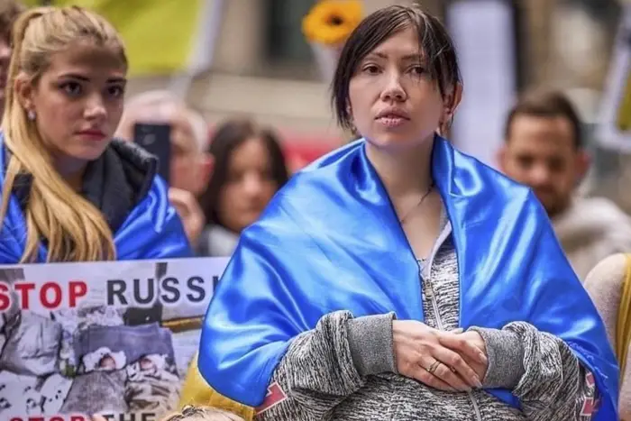 A woman and a child standing in a crowd. They are wrapped in Ukrainian flags.